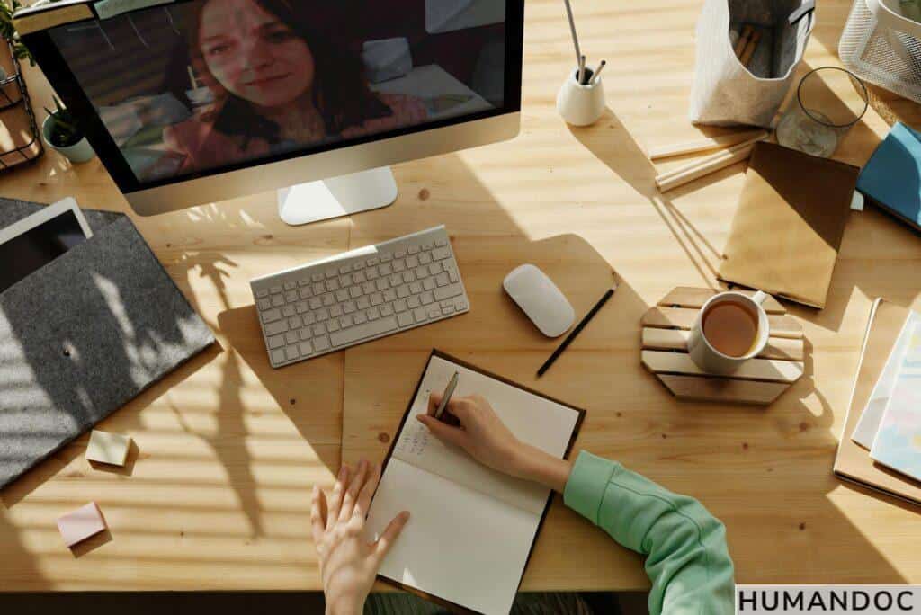 A student taking notes during a video call for online learning at home.