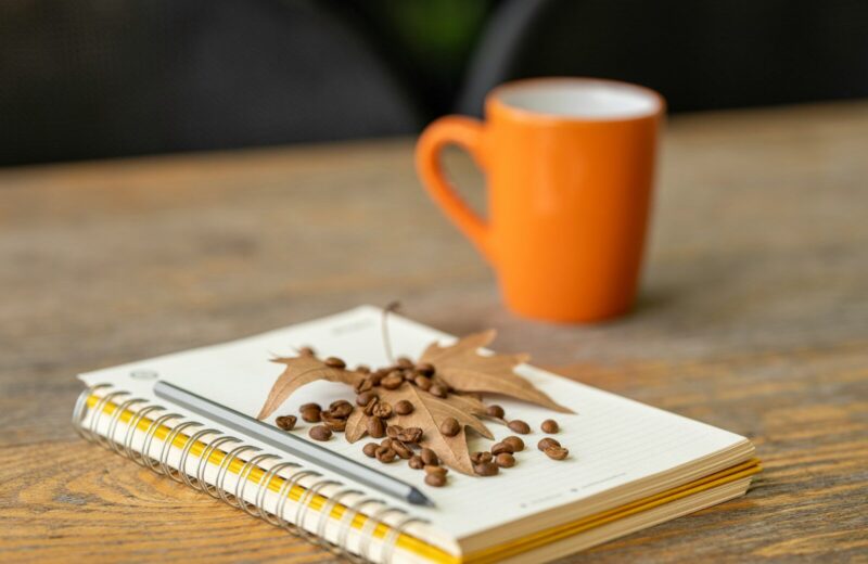 Libreta abierta junto a una taza naranja sobre una mesa de madera